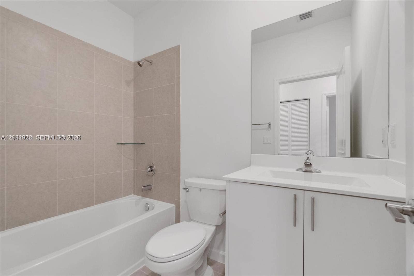 16281 SW 292nd Street, Homestead, FL 33033 Bathroom featuring a white vanity cabinet with a stone countertop, an integrated sink with a chrome faucet, a frameless wall-mounted mirror, and a tub-shower combination with neutral tile surround