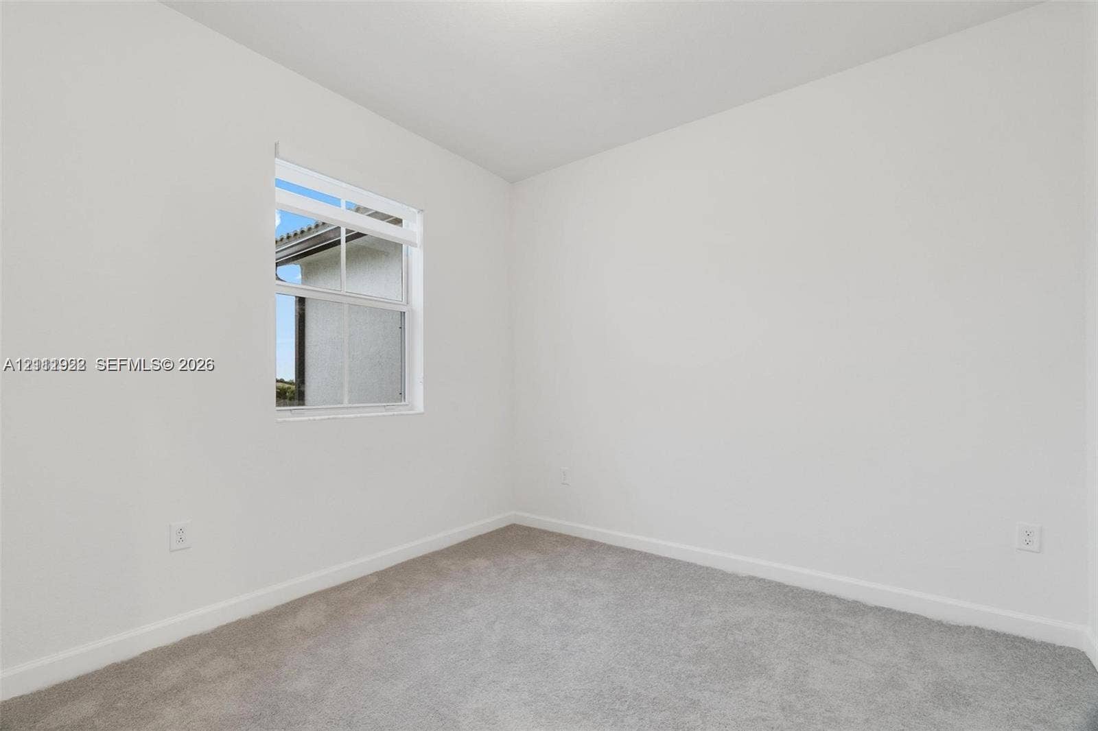 16281 SW 292nd Street, Homestead, FL 33033 Neutral interior space featuring high-contrast white walls, textured wall-to-wall carpeting, and a single-hung window with a grid pattern