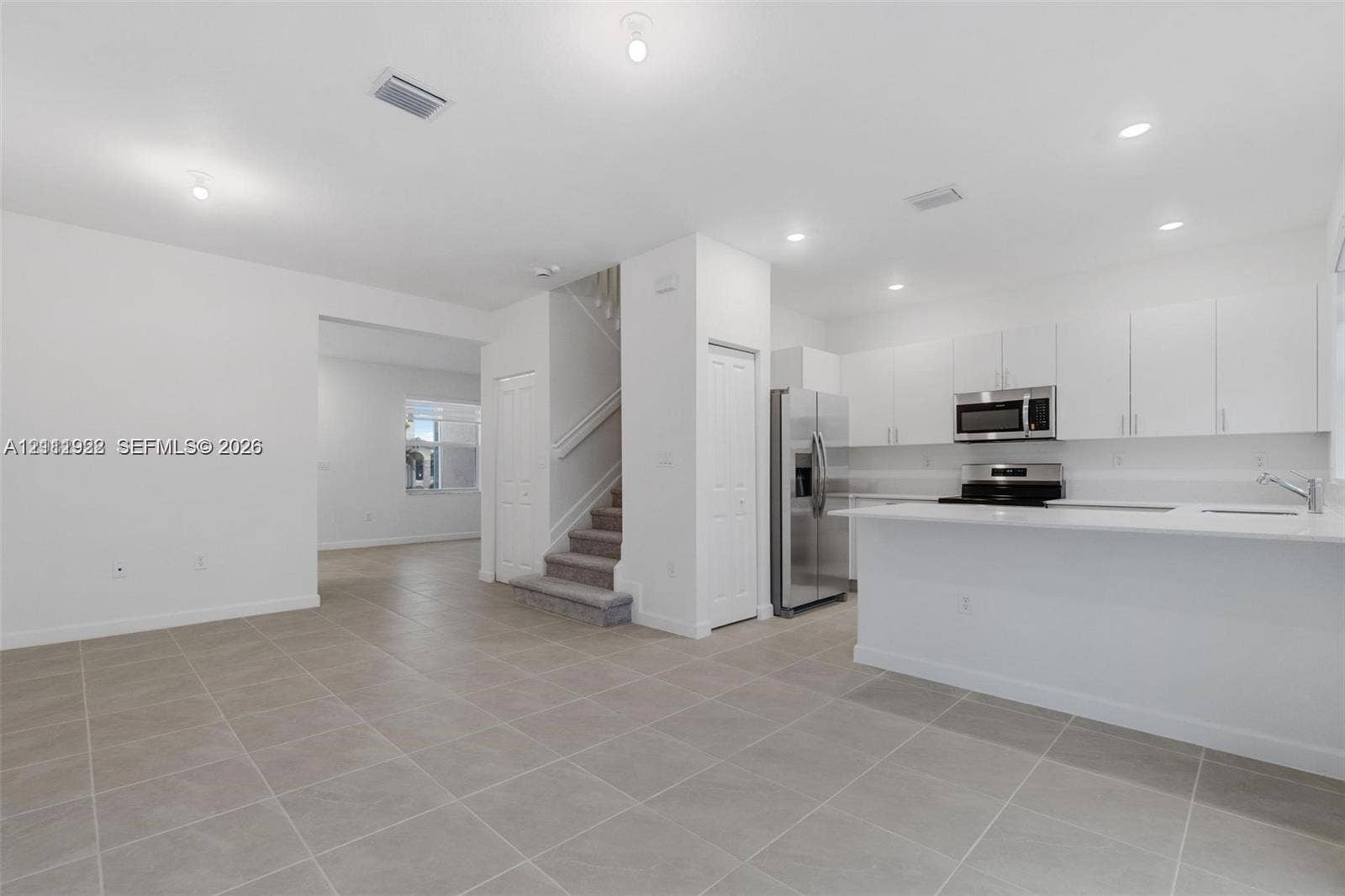 16281 SW 292nd Street, Homestead, FL 33033 Open-concept kitchen featuring white cabinetry, a stone-surface breakfast bar, and stainless steel appliances, set against large-format tile flooring and recessed lighting