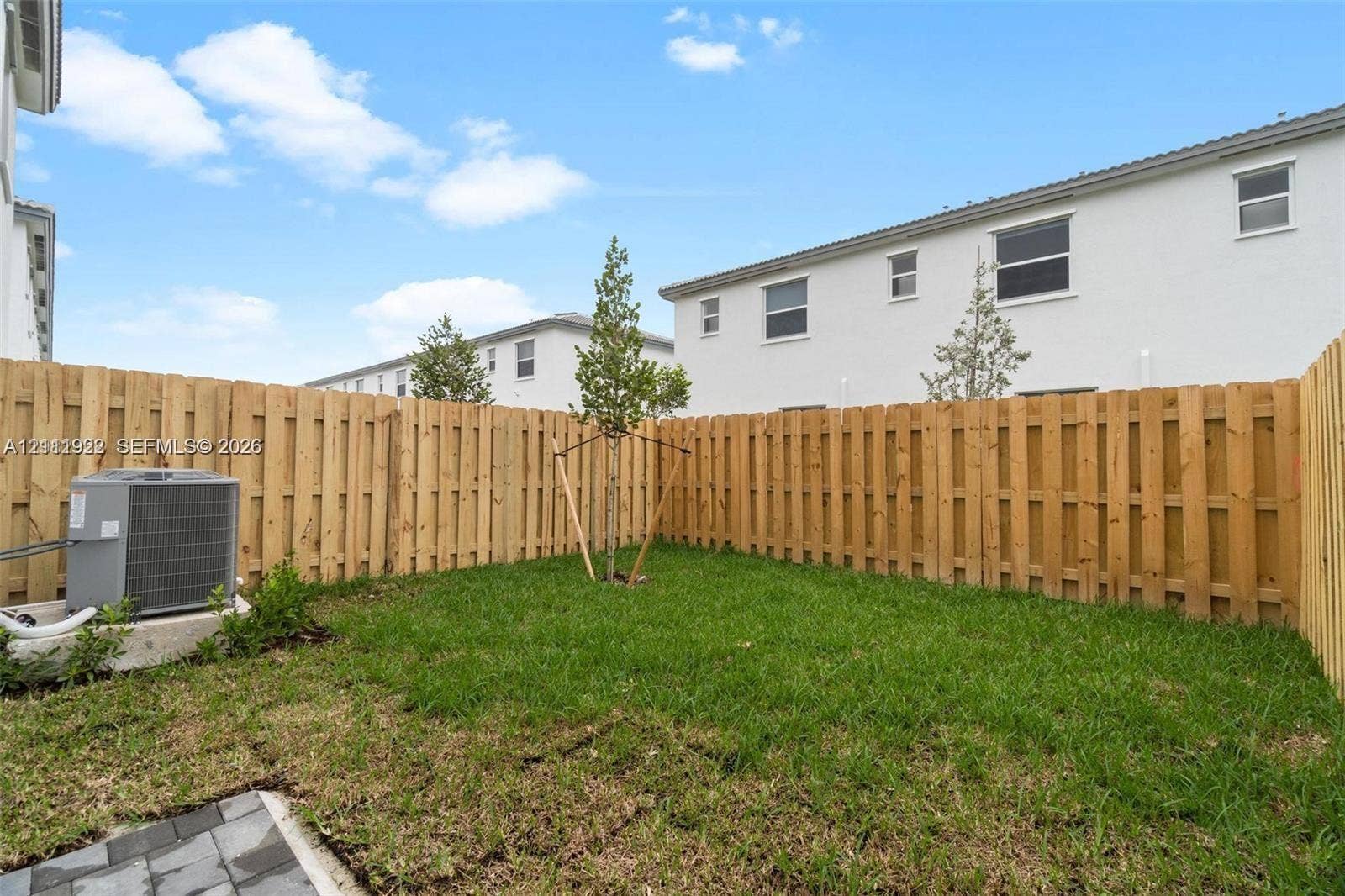 16281 SW 292nd Street, Homestead, FL 33033 Enclosed backyard featuring a privacy wood fence, manicured lawn, young tree, and paver hardscaping