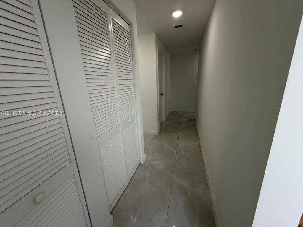 Hallway featuring large-format tile flooring and white louvered-door closet cabinetry