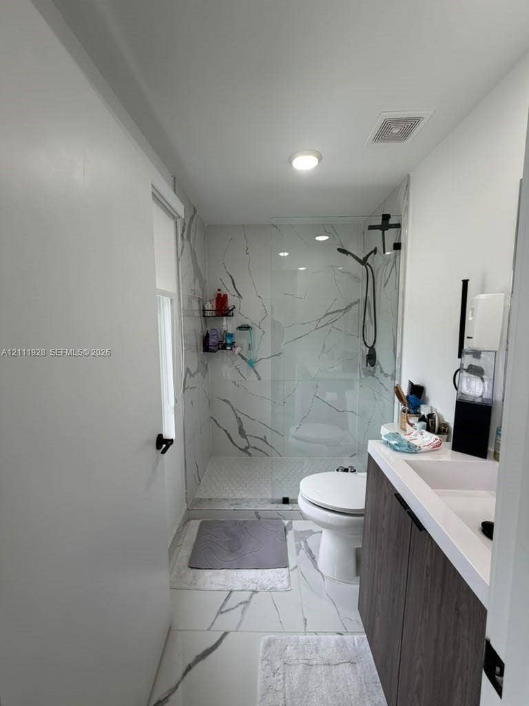 Bathroom featuring large-format tile flooring with marble-finish veining, a walk-in shower with a frameless glass enclosure, and a wood-finish vanity with a white countertop