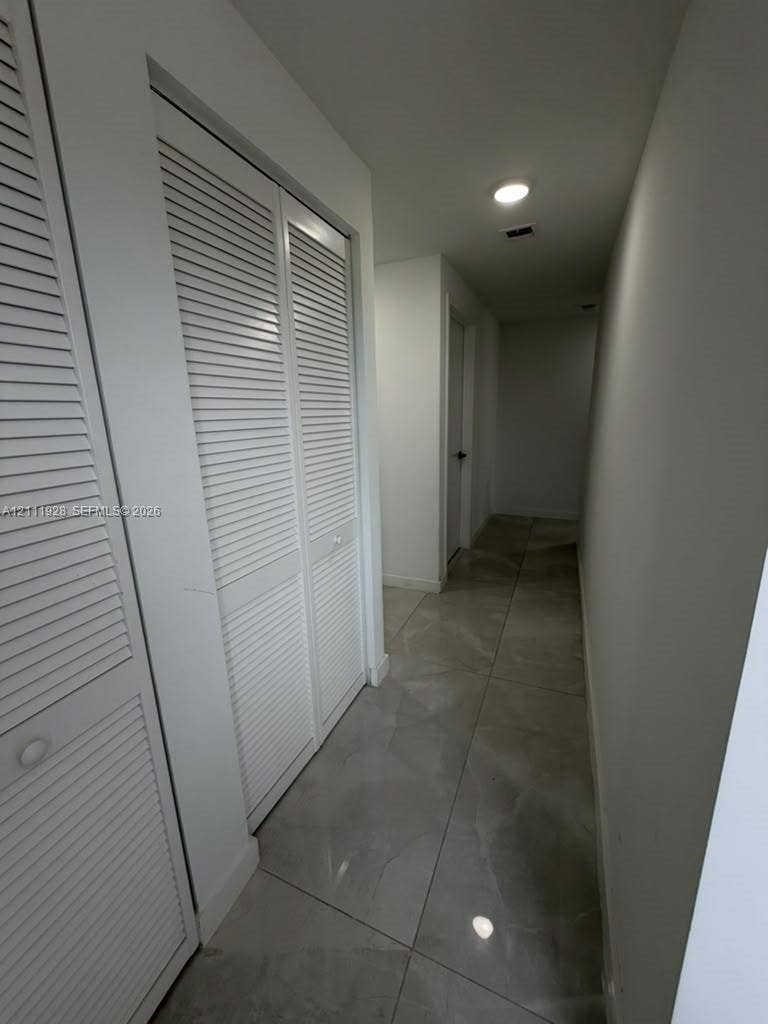 Hallway featuring large-format neutral tile flooring, white walls, and built-in closet cabinetry with louvered doors