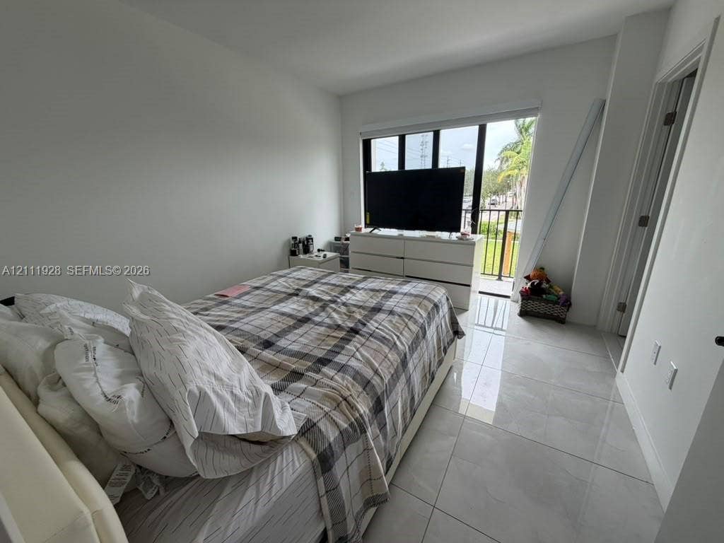 Room featuring large-format tile flooring, floor-to-ceiling windows, and a sliding glass door providing access to a private balcony