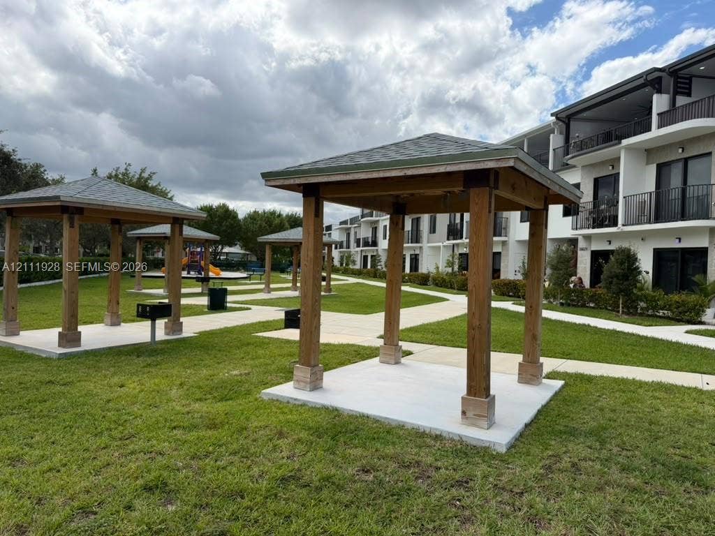 Exterior grounds featuring multiple wood-post gazebos, shingled roofing, concrete pads, and integrated charcoal grills set within a landscaped lawn