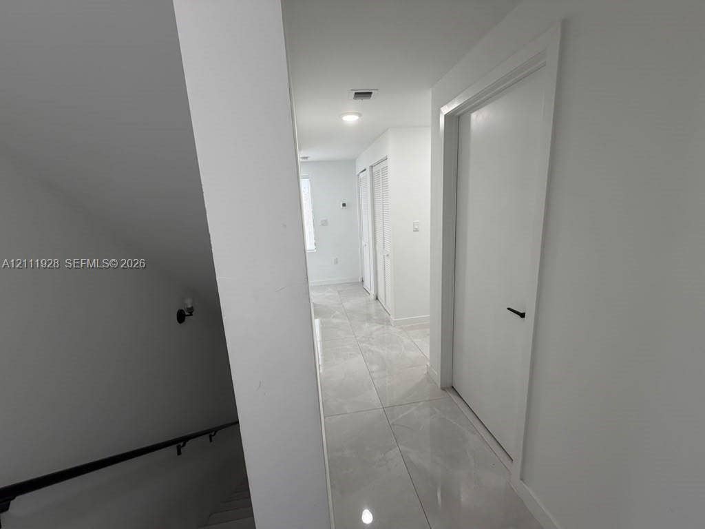 Large-format neutral stone-style tile flooring, solid-core doors with matte black hardware, and recessed lighting