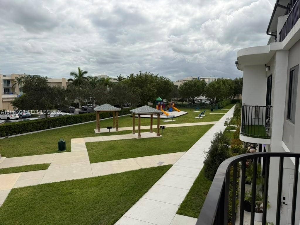 Ground-level exterior space featuring manicured lawn areas, paved walkways, multiple wooden pavilions, and established greenery