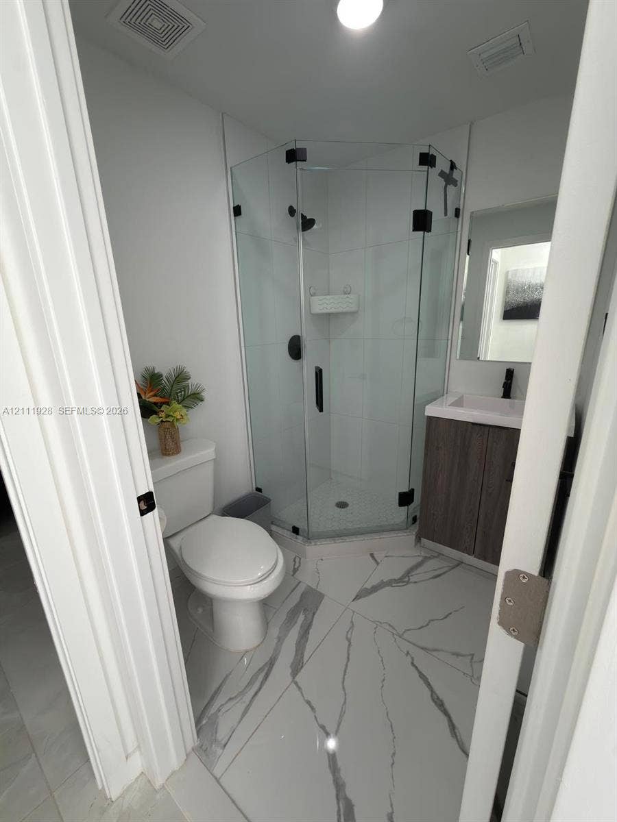 Corner shower stall with glass enclosure and matte black hardware, vanity with stone-pattern countertop, and large-format porcelain tile flooring