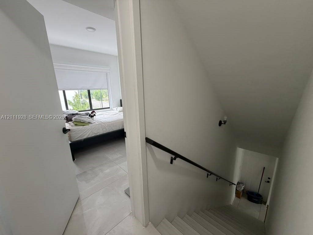Neutral-toned interior featuring large-format tile flooring, a staircase with a matte black handrail, and recessed lighting
