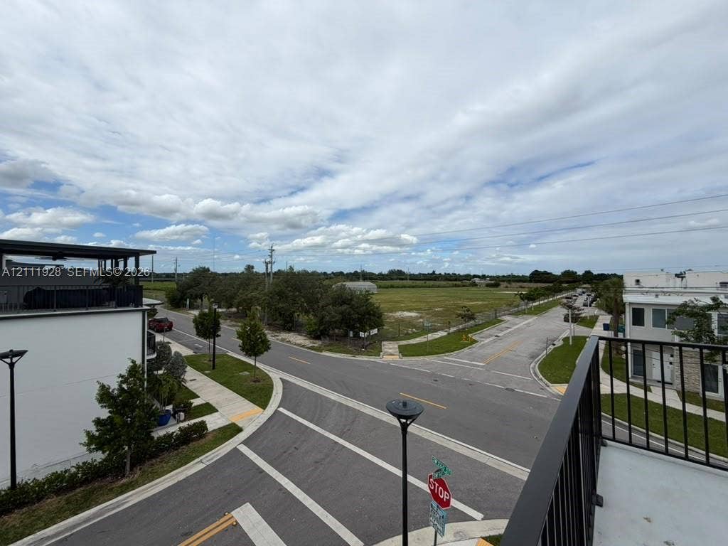 Elevated balcony featuring black metal railings and concrete flooring, overlooking an intersection with paved streets, concrete sidewalks, and street lighting