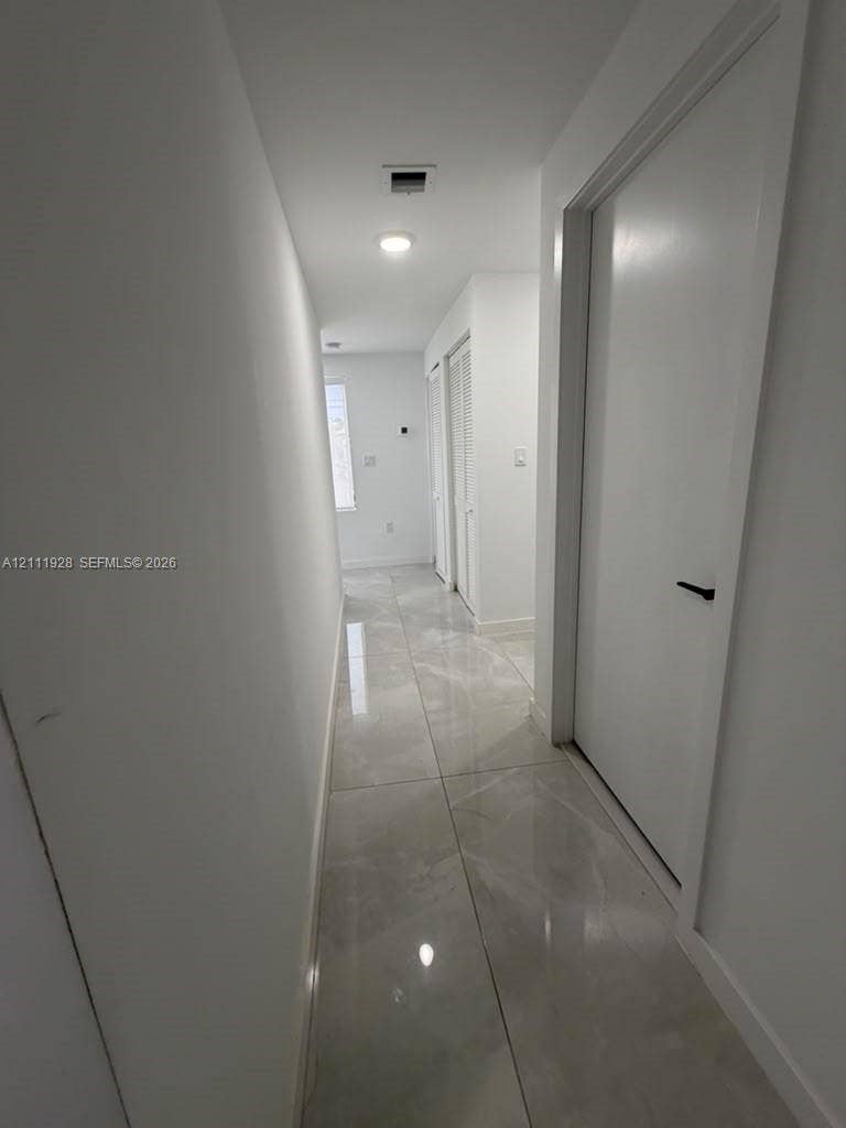 Hallway featuring large-format polished tile flooring, recessed lighting, and interior doors with matte black hardware