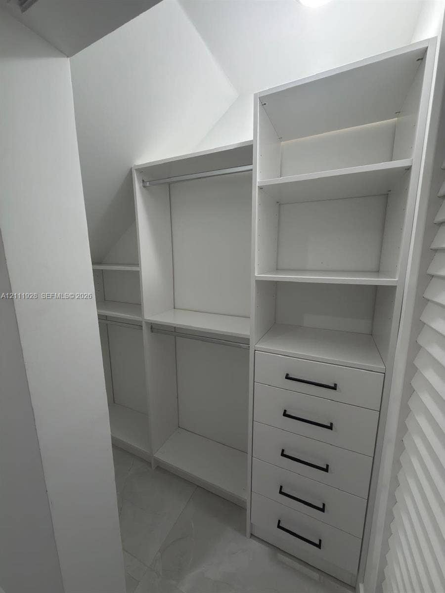 Custom walk-in closet featuring white built-in shelving, a five-drawer dresser unit, hanging rods, and matte black hardware
