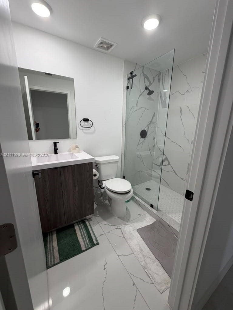 Bathroom featuring a glass-enclosed shower with floor-to-ceiling stone-style wall tile, white vanity with dark wood-finish cabinetry, rectangular vessel sink, and matte black fixtures