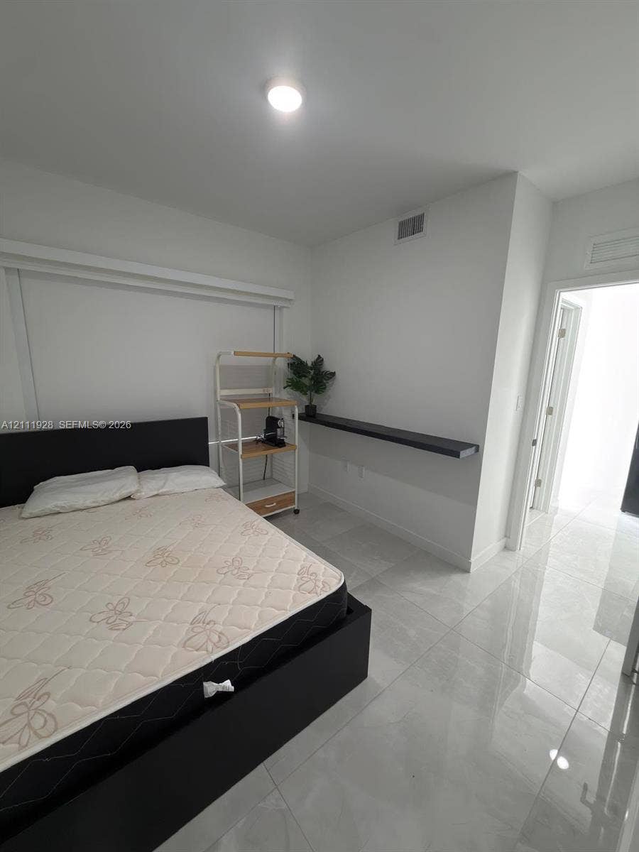 Neutral interior room featuring large-format tile flooring, a wall-mounted floating shelf, and a recessed ceiling light fixture