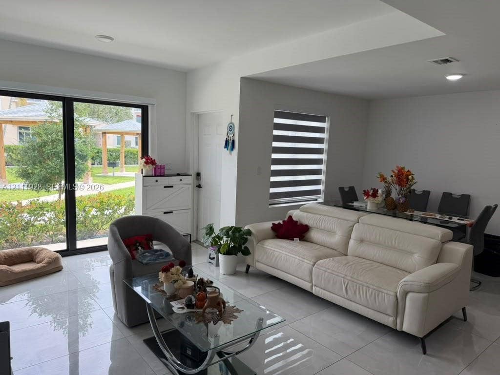 Open-concept interior featuring large-format polished tile flooring, recessed lighting, floor-to-ceiling sliding glass doors, and dual-layered window shades