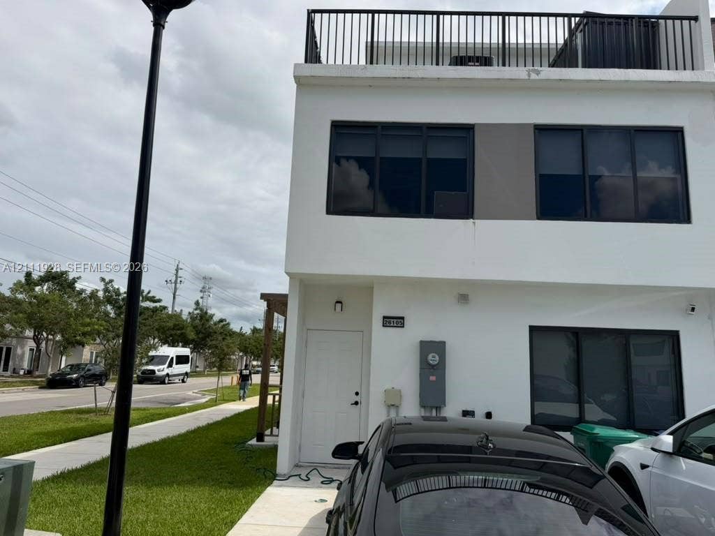 Contemporary exterior featuring a white smooth-stucco facade, flat roofline, third-level terrace with metal railing, and dark-framed multi-pane windows
