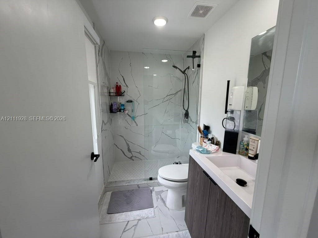 Walk-in shower with floor-to-ceiling stone-pattern tile, frameless glass enclosure, wood-finish vanity with integrated rectangular sink, and matte black hardware