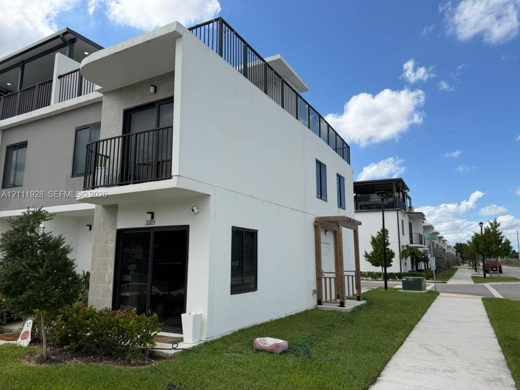 Modern townhome exterior featuring a rooftop deck with metal railings, a private second-story balcony, sliding glass doors, and a decorative wood-post entryway