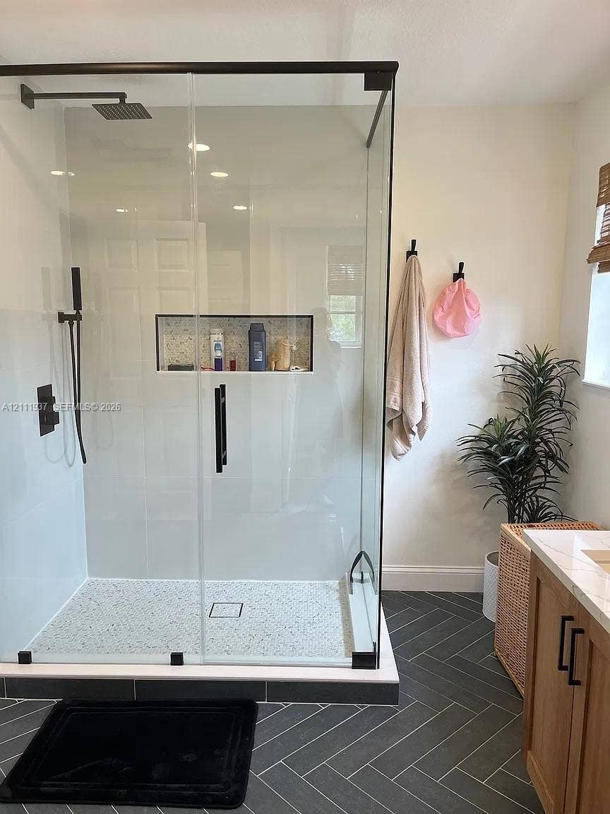 869 Nandina Drive, #869, Weston, Weston, FL 33327 Walk-in shower featuring a glass enclosure with matte black hardware, a rainfall showerhead, a handheld sprayer, and a recessed tiled niche, complemented by charcoal-toned herringbone floor tiling