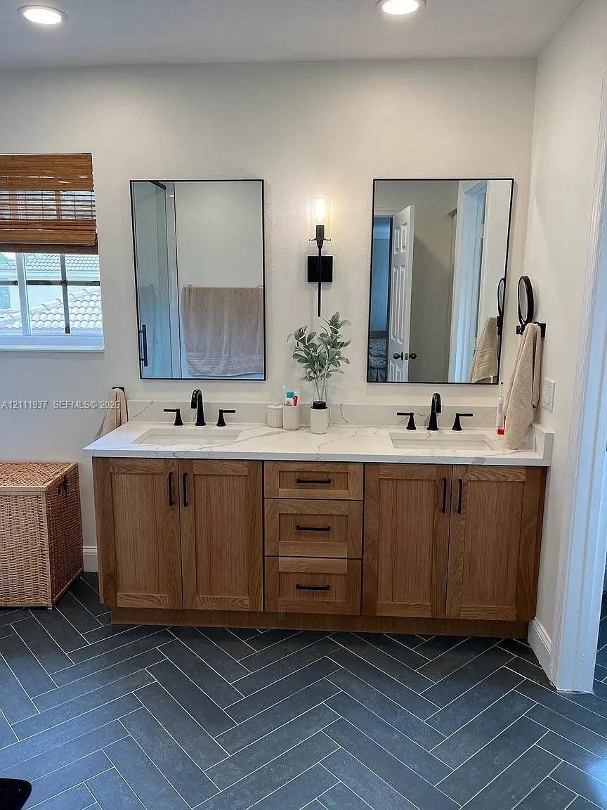 869 Nandina Drive, #869, Weston, Weston, FL 33327 Double vanity with a stone countertop, under-mount sinks, wood cabinetry, matte black hardware, and herringbone-patterned tile flooring