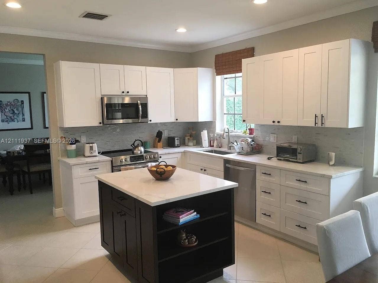 869 Nandina Drive, #869, Weston, Weston, FL 33327 Kitchen featuring white shaker-style cabinetry, contrasting dark-toned kitchen island with open shelving, neutral-toned stone countertops, subway tile backsplash, and stainless steel appliances