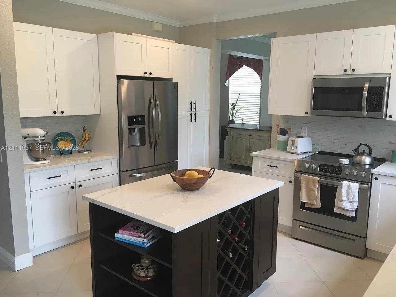 869 Nandina Drive, #869, Weston, Weston, FL 33327 Kitchen featuring white shaker-style cabinetry, a central island with built-in wine storage and open shelving, light-toned stone-finish countertops, stainless steel appliances, and a tiled backsplash