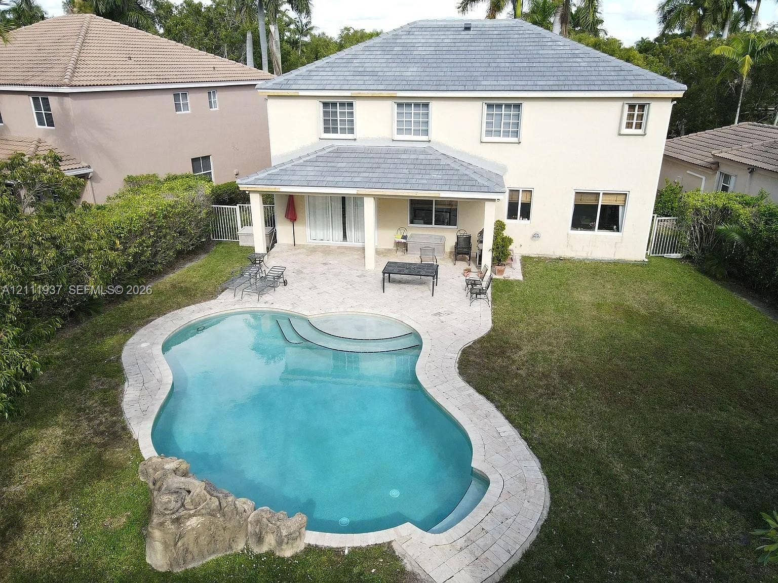 869 Nandina Drive, #869, Weston, Weston, FL 33327 Rear exterior featuring a covered patio, paved pool deck, freeform swimming pool with integrated rock feature, and a manicured lawn