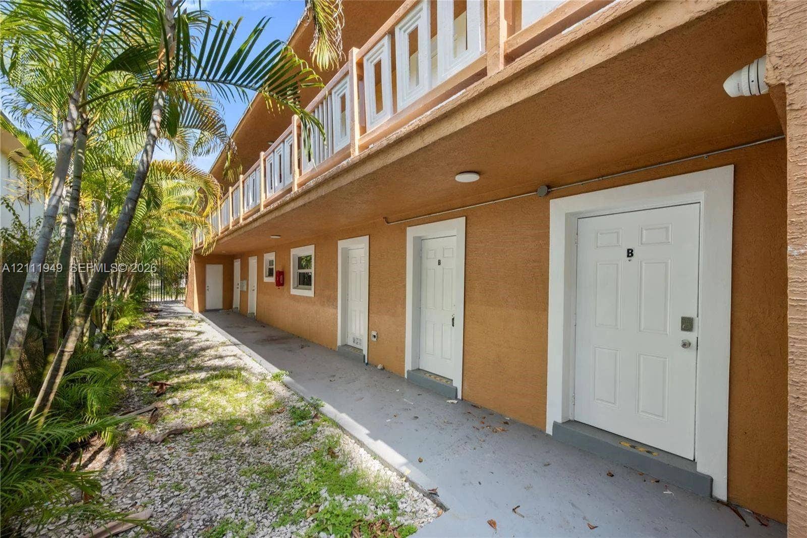 Two-story exterior featuring textured stucco finish, exterior walkway, second-level balcony with white railing, and flush-mount lighting fixtures