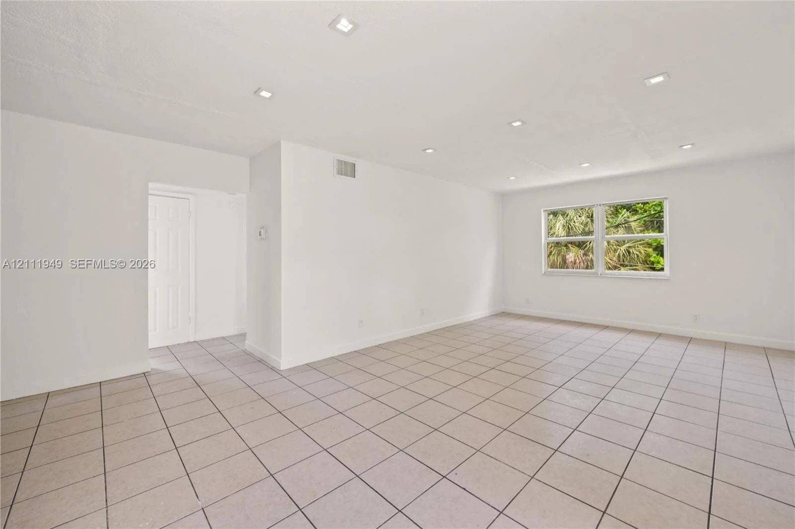 Open interior space featuring neutral ceramic tile flooring, recessed ceiling lighting, and a single-pane window