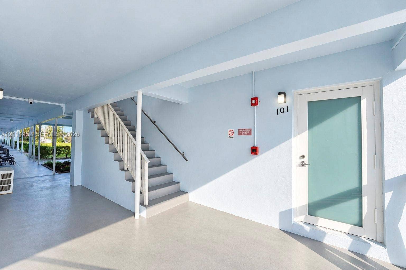 Covered entryway featuring a frosted impact glass entry door, painted concrete flooring, and an exterior staircase with metal railing