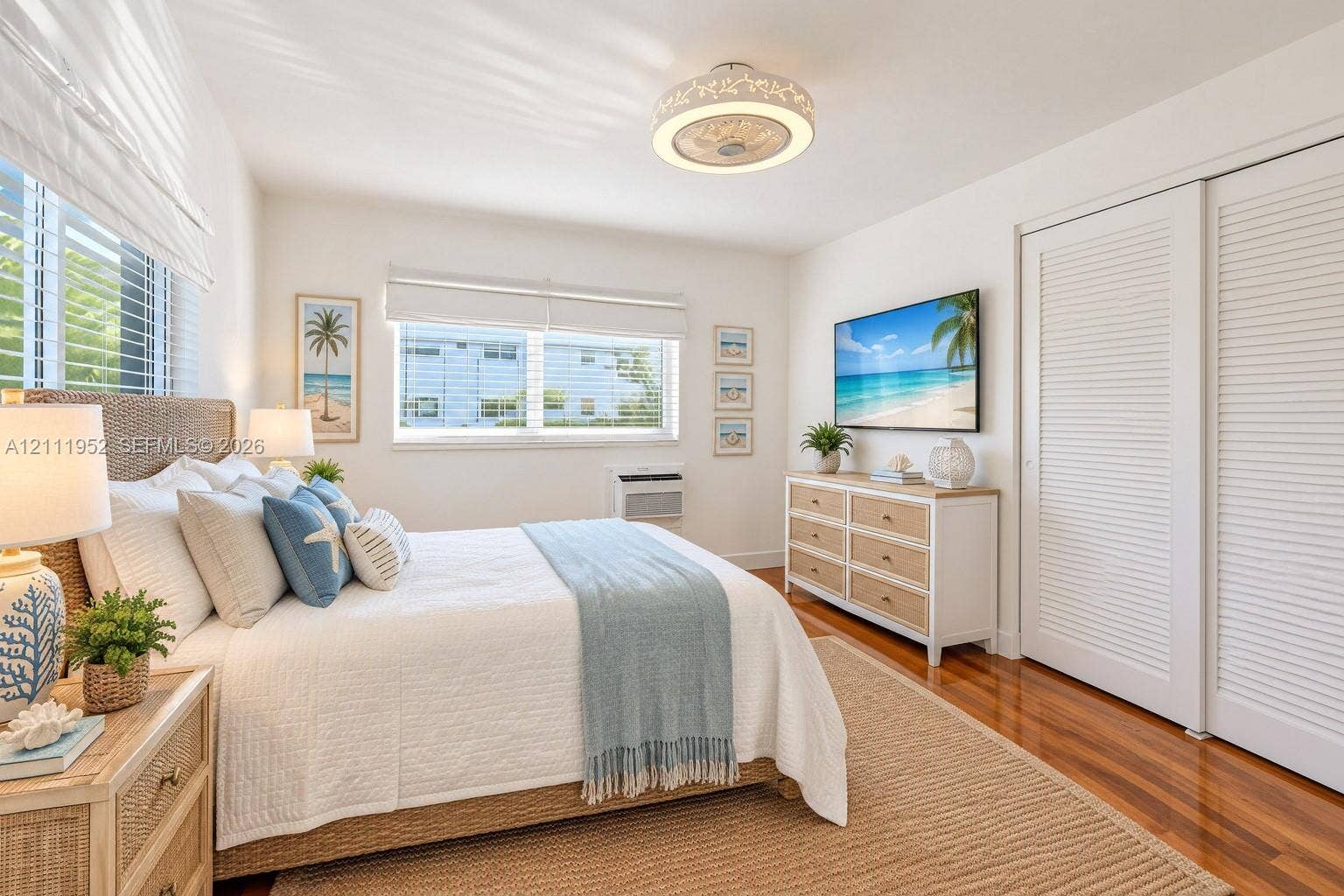 Wood flooring, white louvered sliding closet doors, impact windows with fitted roman shades, and a decorative circular LED lighting fixture with internal fan.