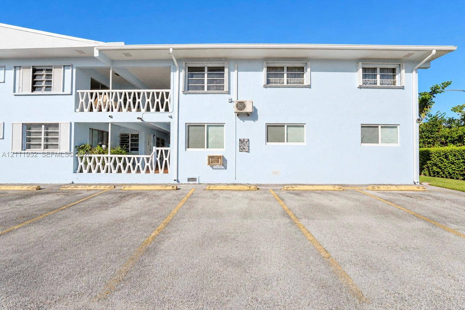 Multi-story exterior featuring a two-level railed balcony, asphalt parking area, and horizontal sliding windows