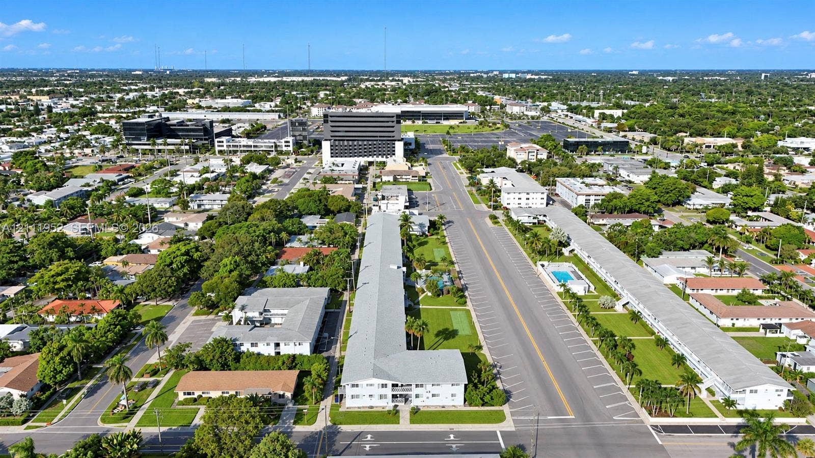Aerial perspective of a multi-story residential building featuring a light-colored exterior finish, a flat roofline, manicured perimeter landscaping, and dedicated surface parking