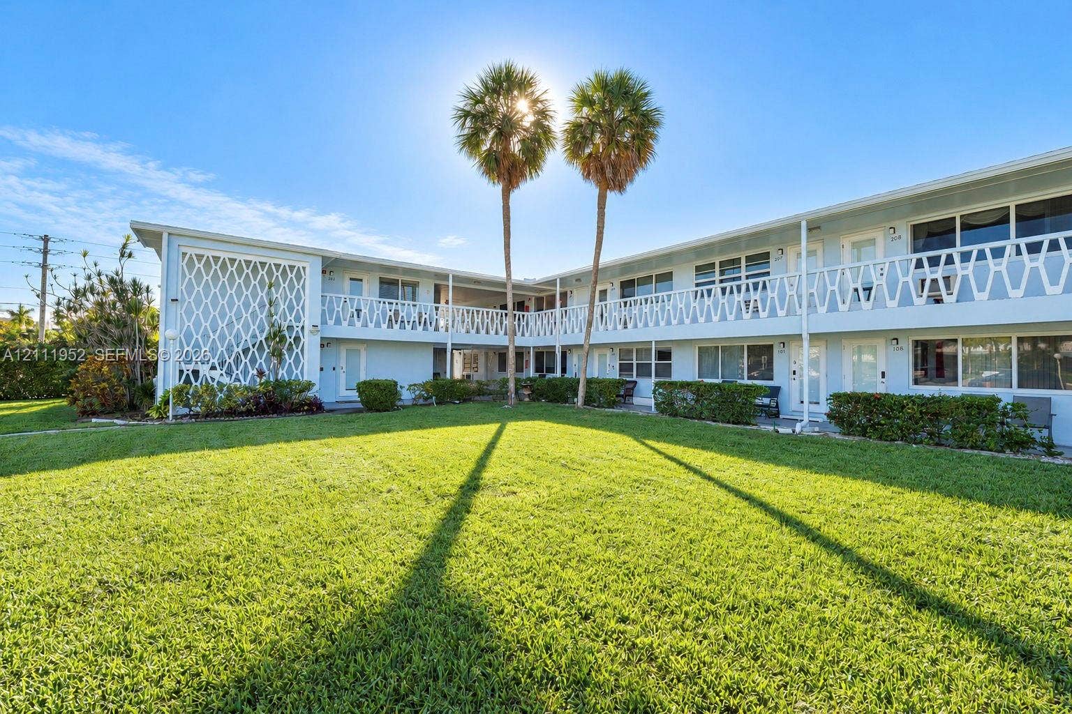 Two-story mid-century modern architecture with exterior featuring white geometric decorative privacy screens, cantilevered balconies with metal railings, and an expansive lawn with mature palm trees