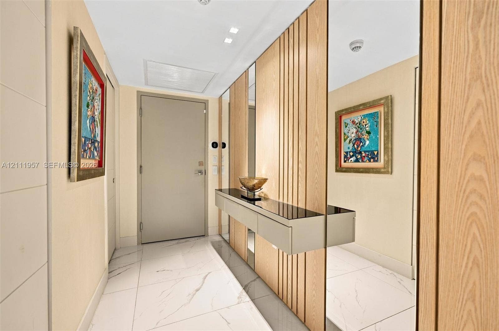 Entryway featuring large-format white tile flooring, vertical wood slat wall paneling, floor-to-ceiling mirror accents, and a built-in wall-mounted console with a dark glass top