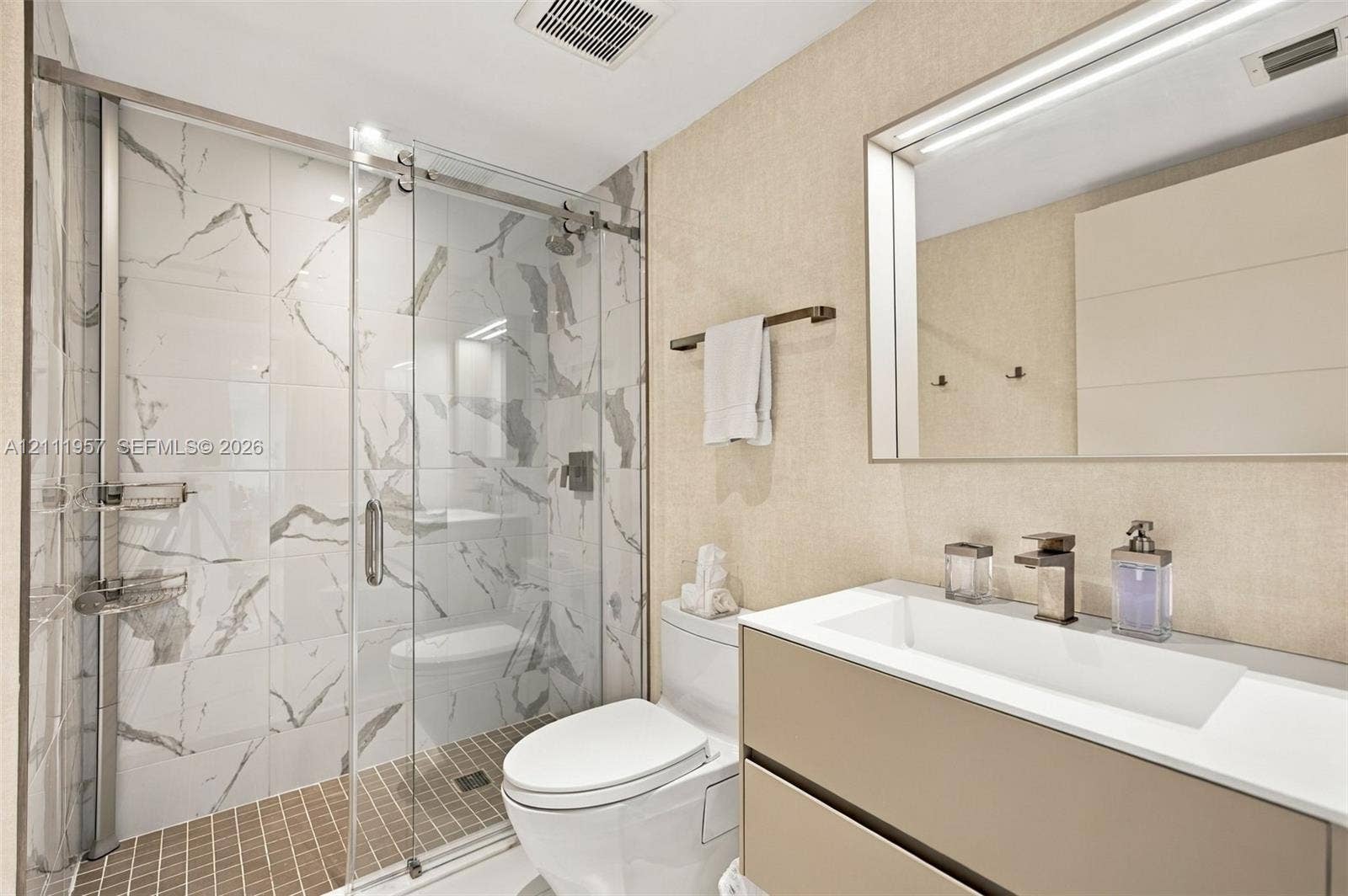 Floating vanity with integrated rectangular sink and metallic faucet, complemented by a walk-in shower featuring sliding glass doors and large-format veined tile surround