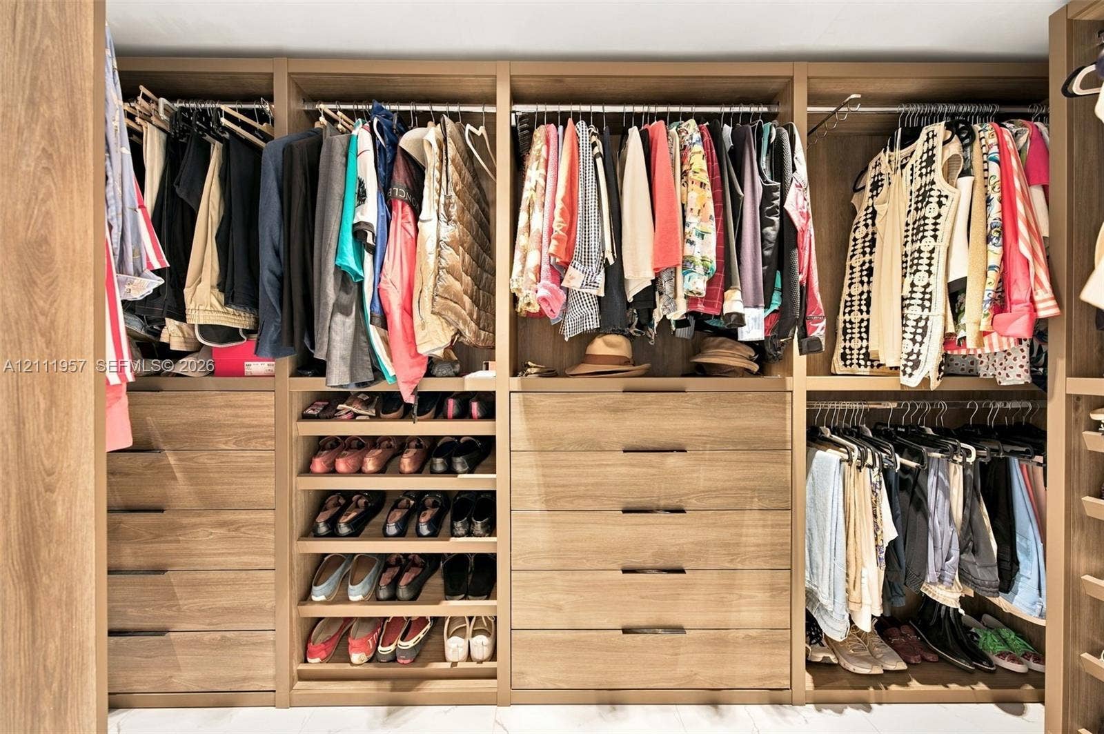 Custom closet organization system featuring wood-finish cabinetry, multi-tiered hanging rods, integrated shelving for footwear, and deep drawers with modern hardware