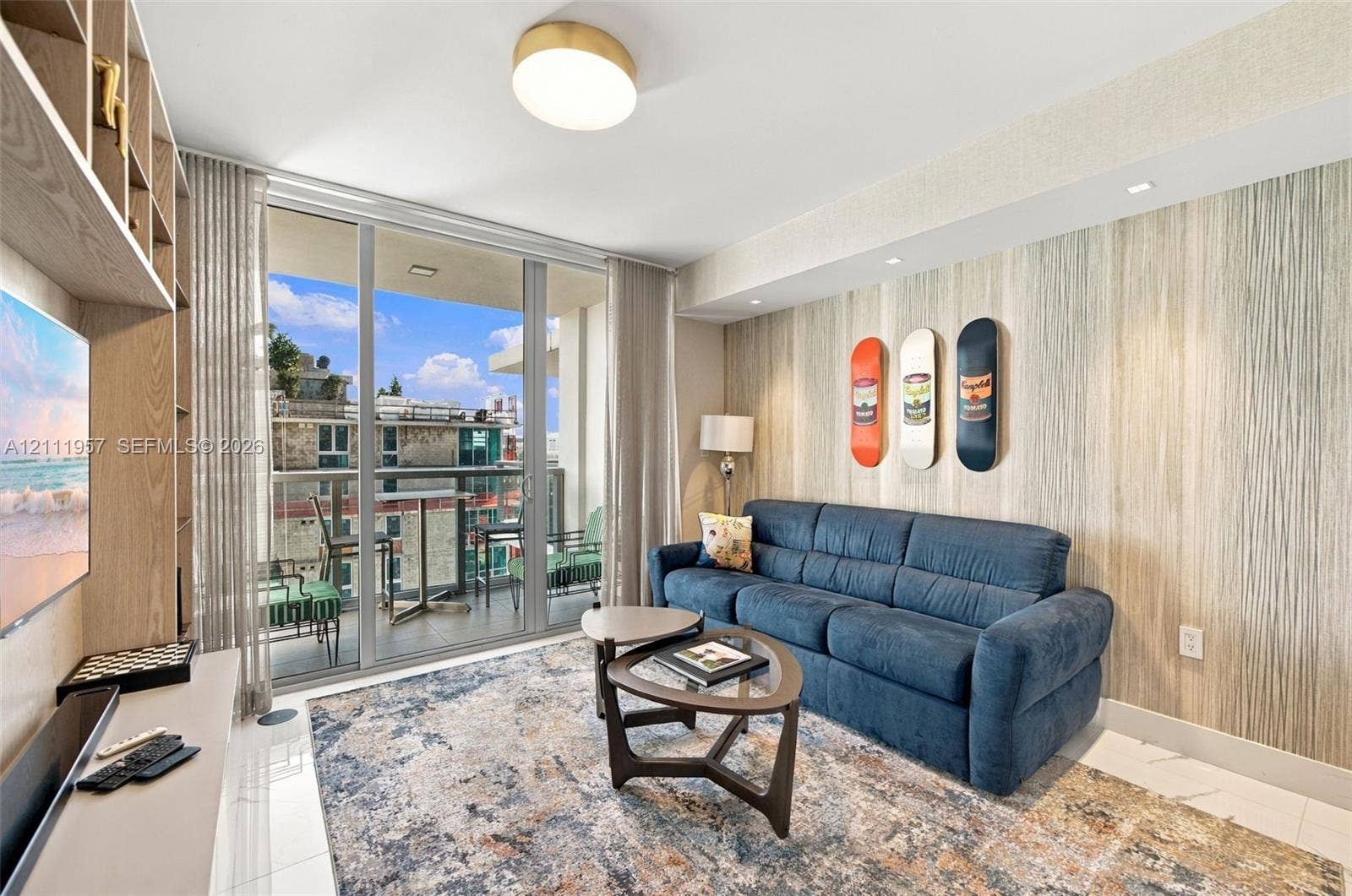 Living area featuring floor-to-ceiling glass sliding doors, built-in open-shelf cabinetry, textured accent wall, polished tile flooring, and flush-mount lighting