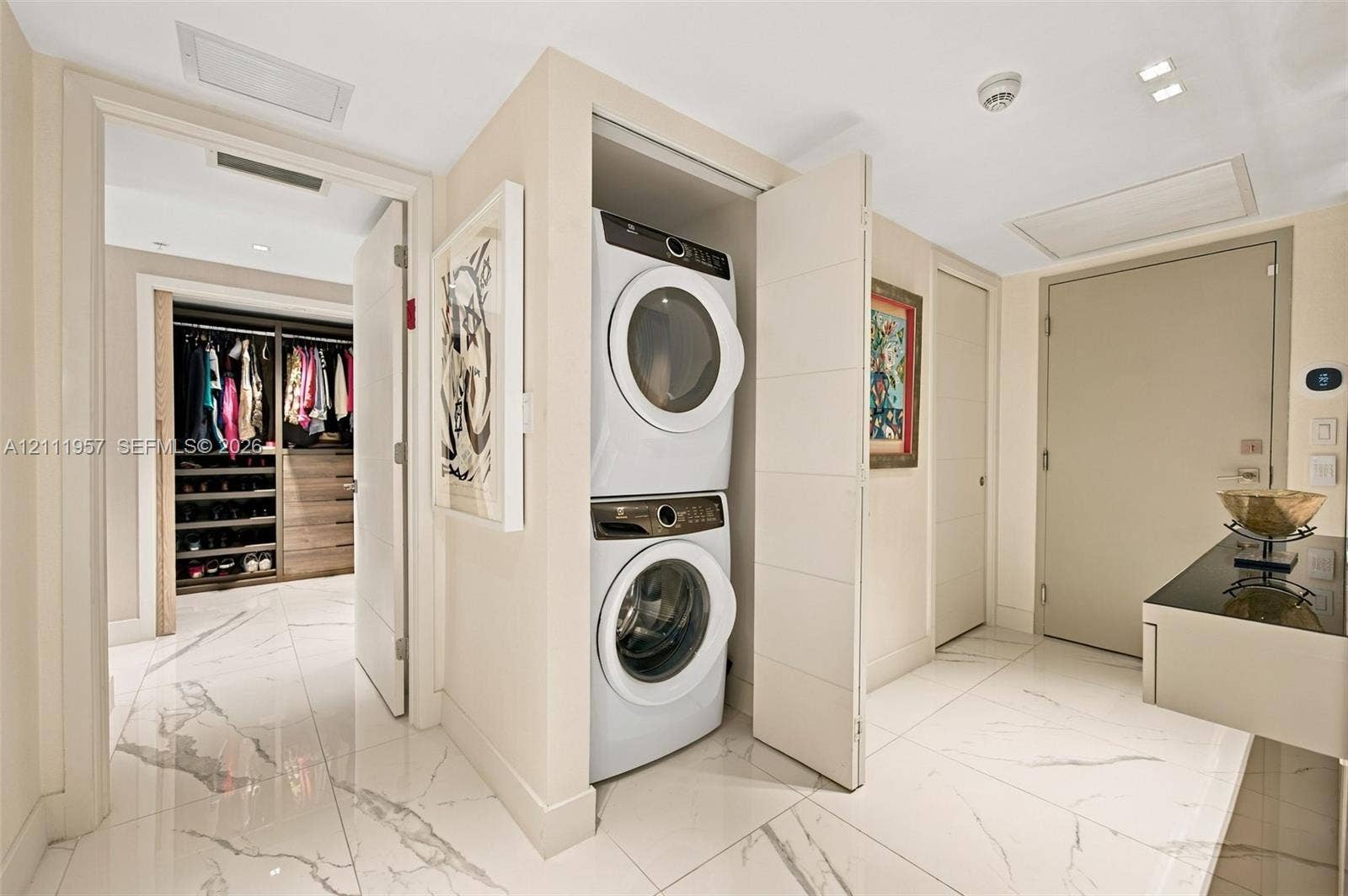 Stacked laundry unit housed in a dedicated closet, polished stone-finish flooring, and built-in closet shelving with integrated drawers