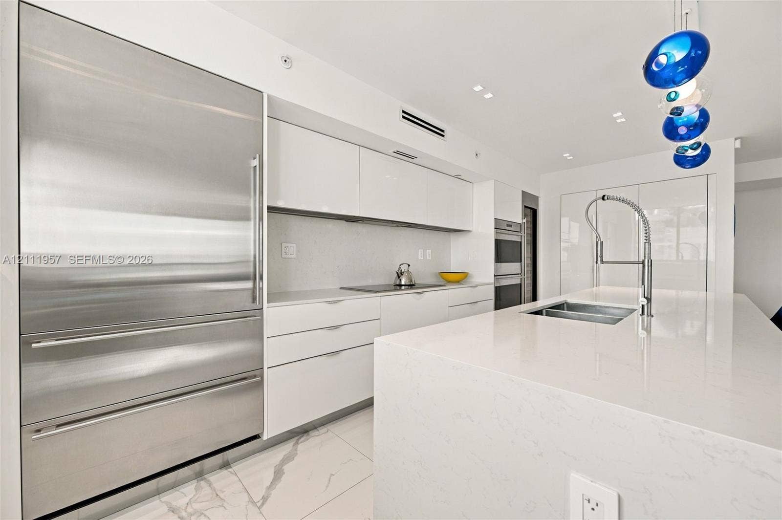 Modern kitchen featuring high-gloss cabinetry, a quartz waterfall island, stone-finish flooring, integrated stainless steel refrigeration, and a commercial-style pull-down faucet