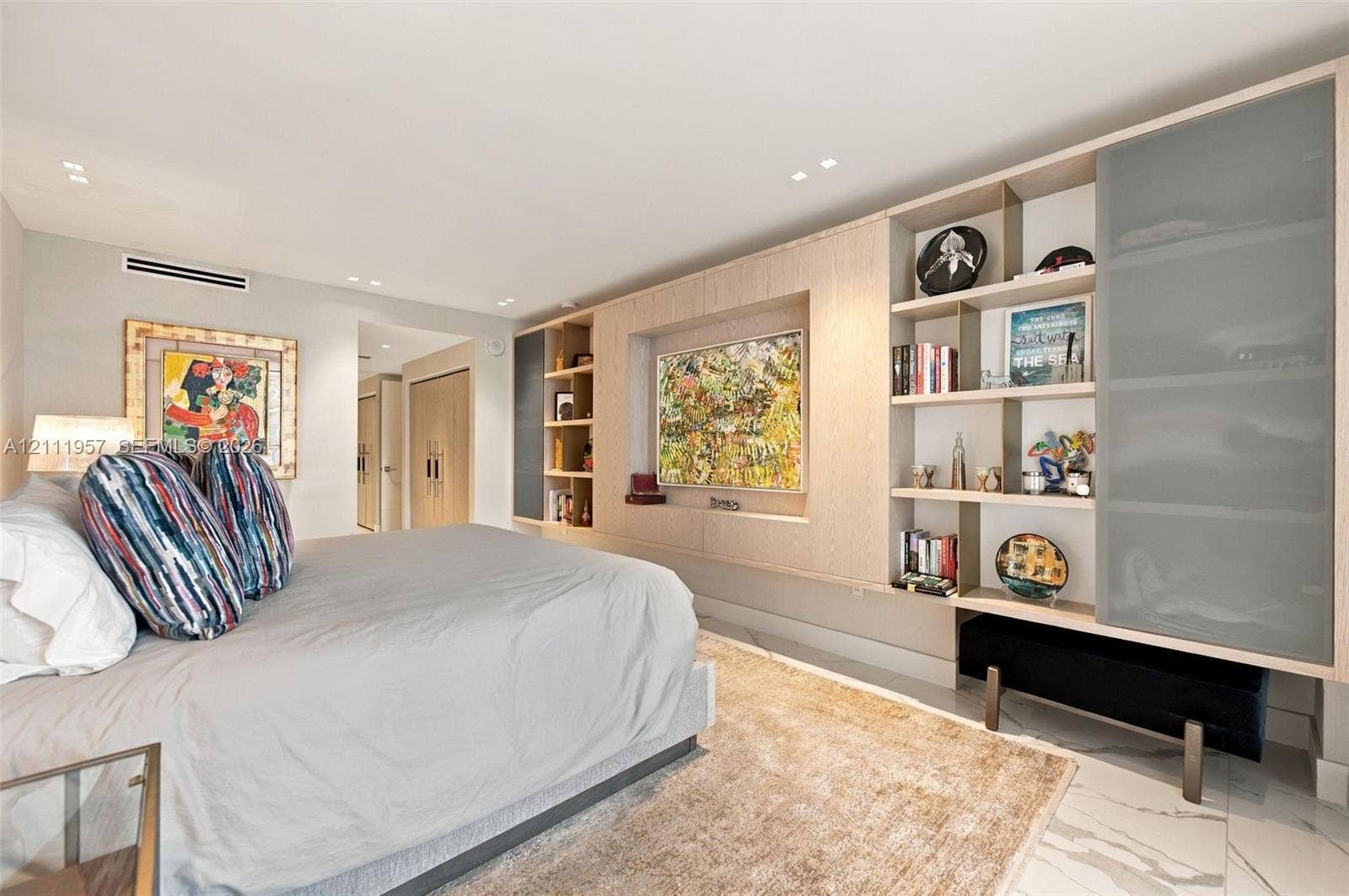 Built-in light wood cabinetry featuring open display shelving and recessed television mount, stone-finish flooring, and recessed ceiling lighting