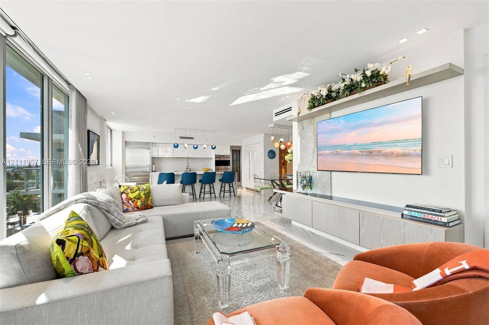 Floor-to-ceiling glass windows, recessed ceiling lighting, stone-finish flooring, custom built-in media cabinetry, and an open-concept kitchen with stainless steel appliances