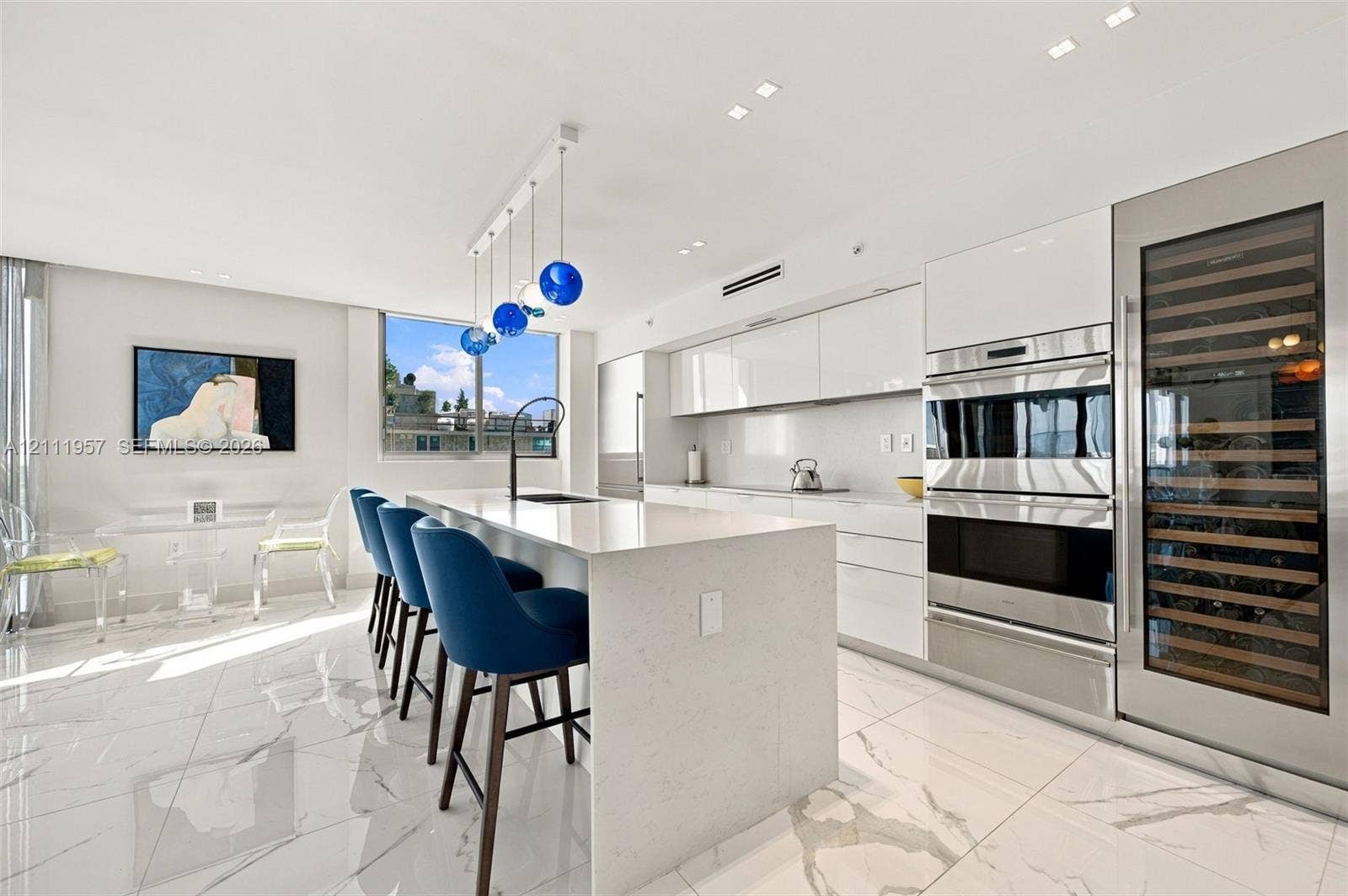 Kitchen featuring high-gloss cabinetry, a waterfall-edge island with a quartz countertop, stone-finish flooring, built-in stainless steel appliances, and integrated wine storage