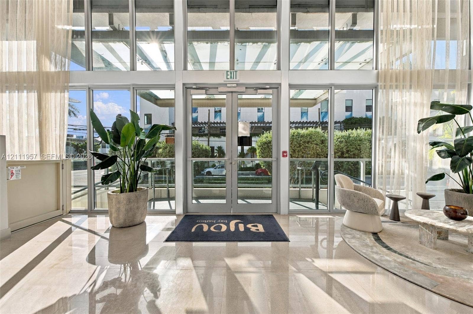 Floor-to-ceiling glass wall, double glass entry doors, expansive polished stone flooring, and high-reaching structural beams