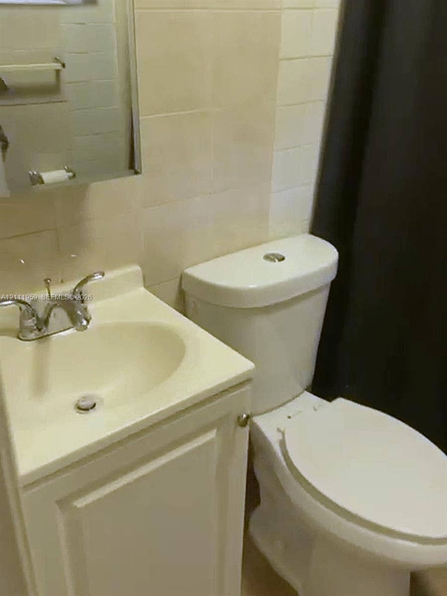 1947 Lincoln Street, #C, Hollywood, Hollywood, FL 33020 Bathroom featuring a white vanity cabinet with an integrated sink, dual-handle chrome faucet, wall-mounted medicine cabinet, and ceramic wall tiling