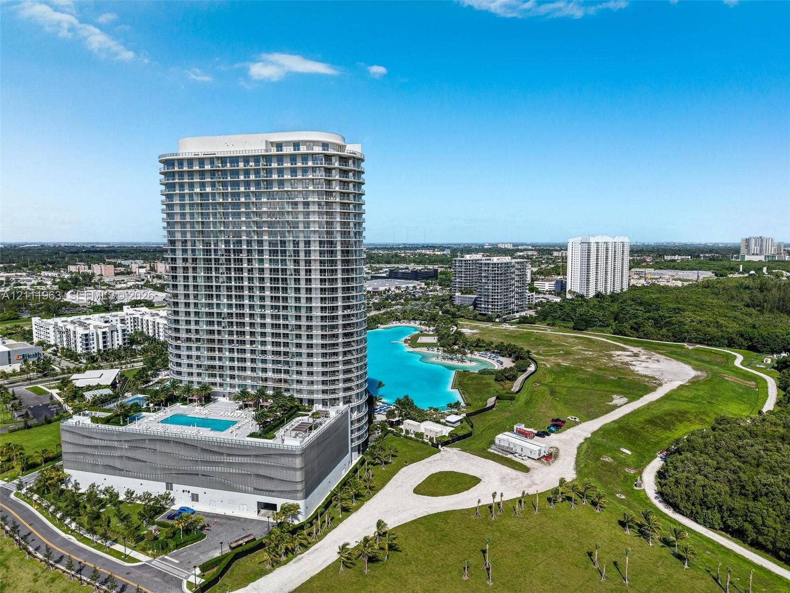 High-rise residential tower featuring floor-to-ceiling glass windows, a multi-level parking structure with an integrated outdoor swimming pool, and proximity to an expansive lagoon