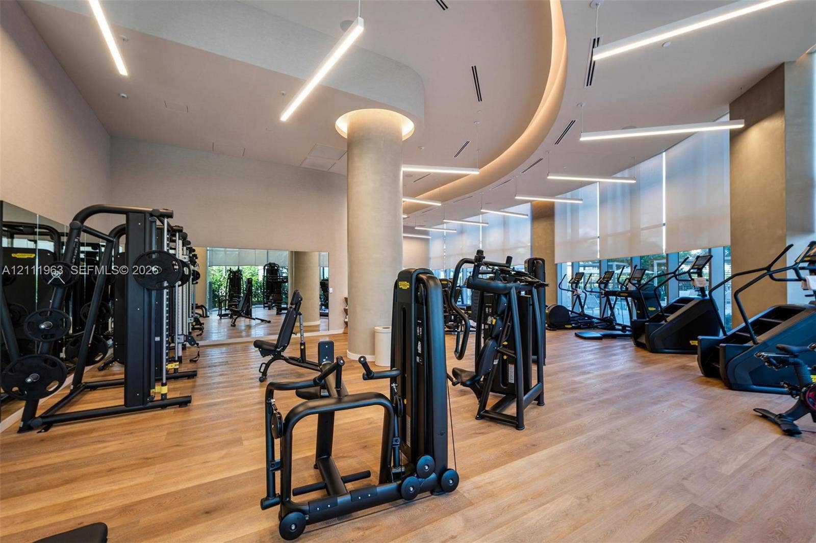 Fitness facility featuring floor-to-ceiling windows, wood-finish flooring, recessed tray ceiling lighting, and large wall-mounted mirrors