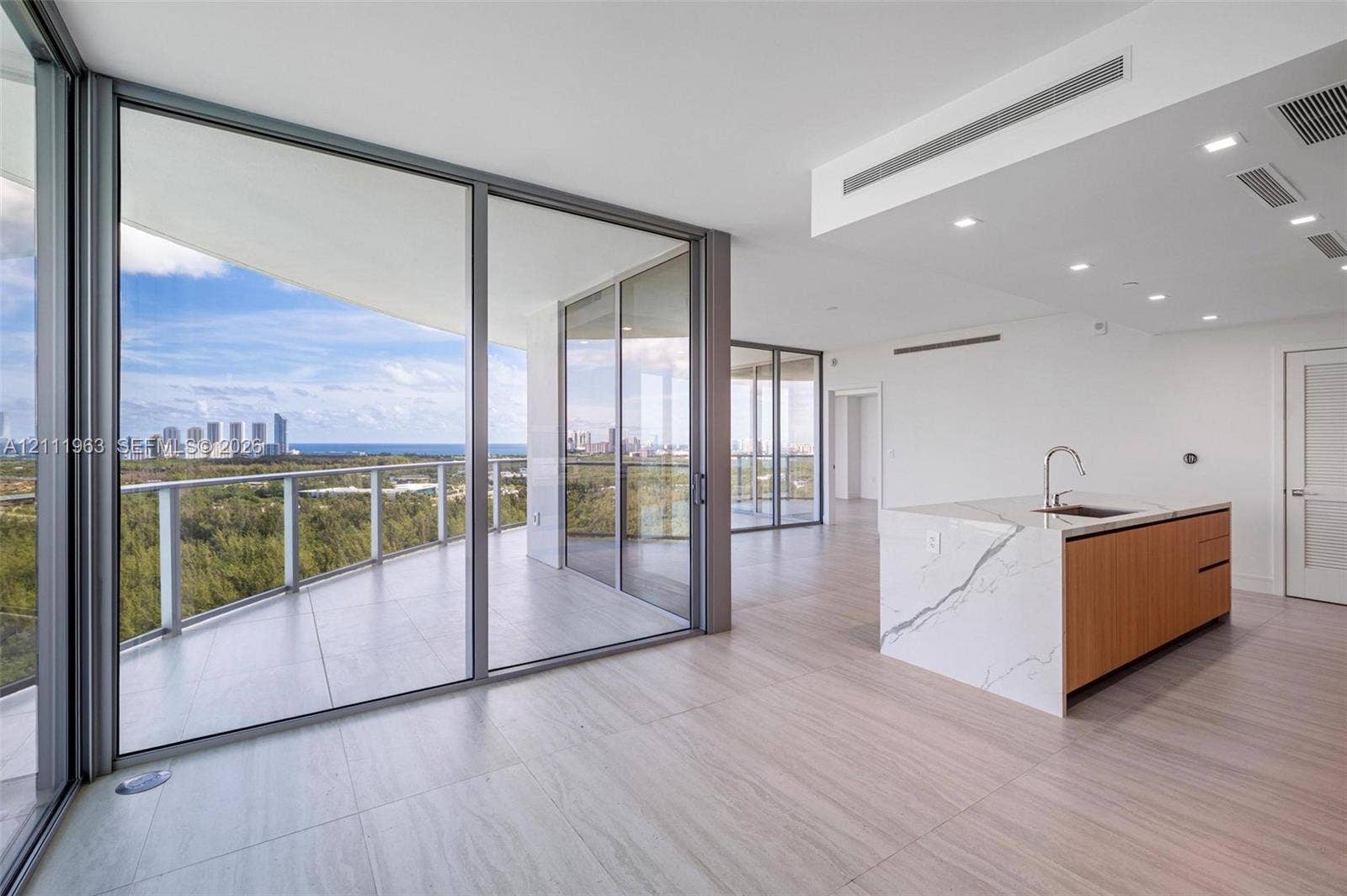 Open-concept kitchen featuring wood-finish cabinetry, white slab cabinetry, stone-surface countertops, recessed lighting, and floor-to-ceiling glass sliding doors