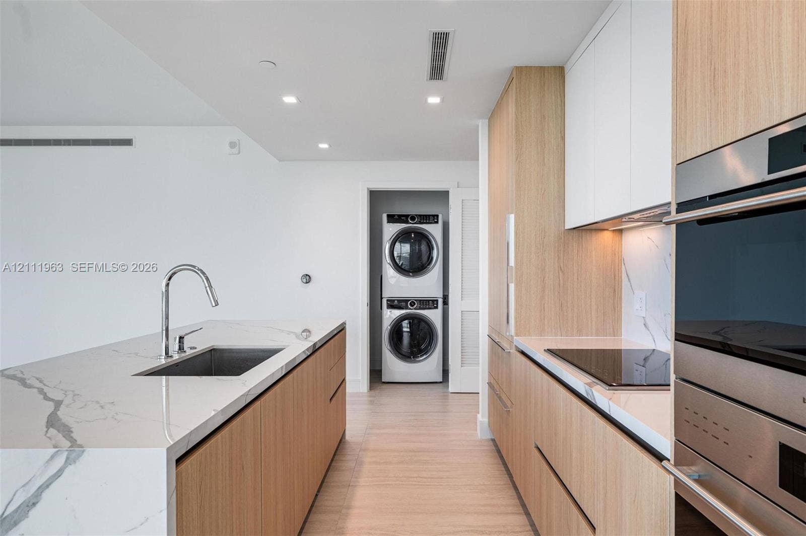 Floor-to-ceiling glass sliding doors, wood-finish cabinetry, built-in double wall oven, light-toned tile flooring, and stone-surfaced island