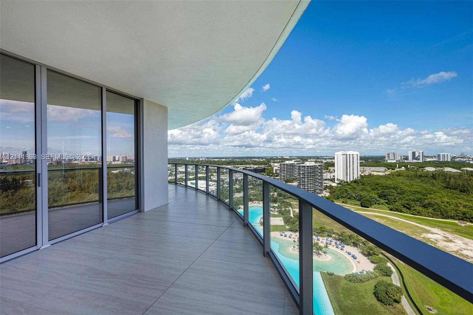 Curved balcony featuring large-format tile flooring and frameless glass railings, overlooking an expansive landscape and coastal horizon